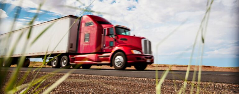Red sleeper cab with dry van trailer drives down highway